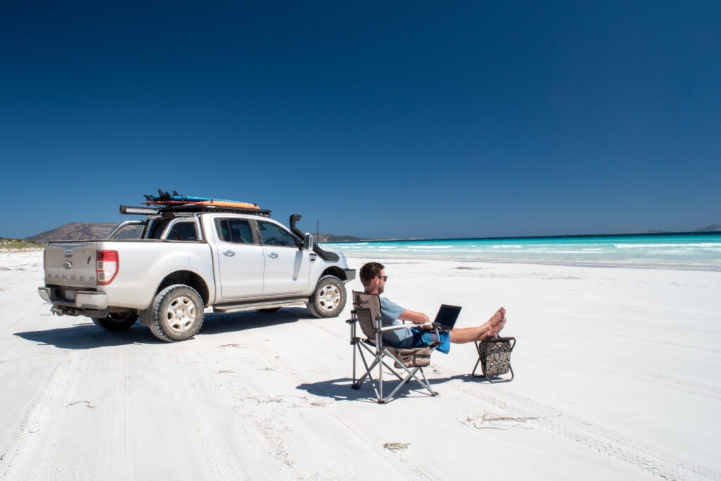 Car, man on computer at white sand beach, Esperance, Western Australia