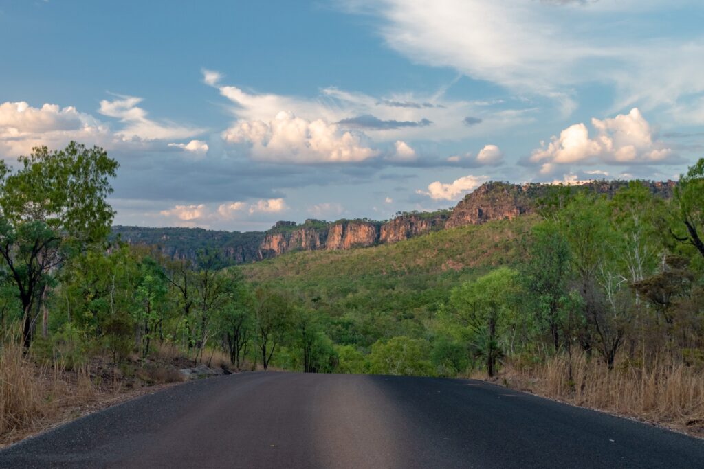 A road in the foreground leads the eye to bushland and an escarpment as it’s lit up by the setting sun