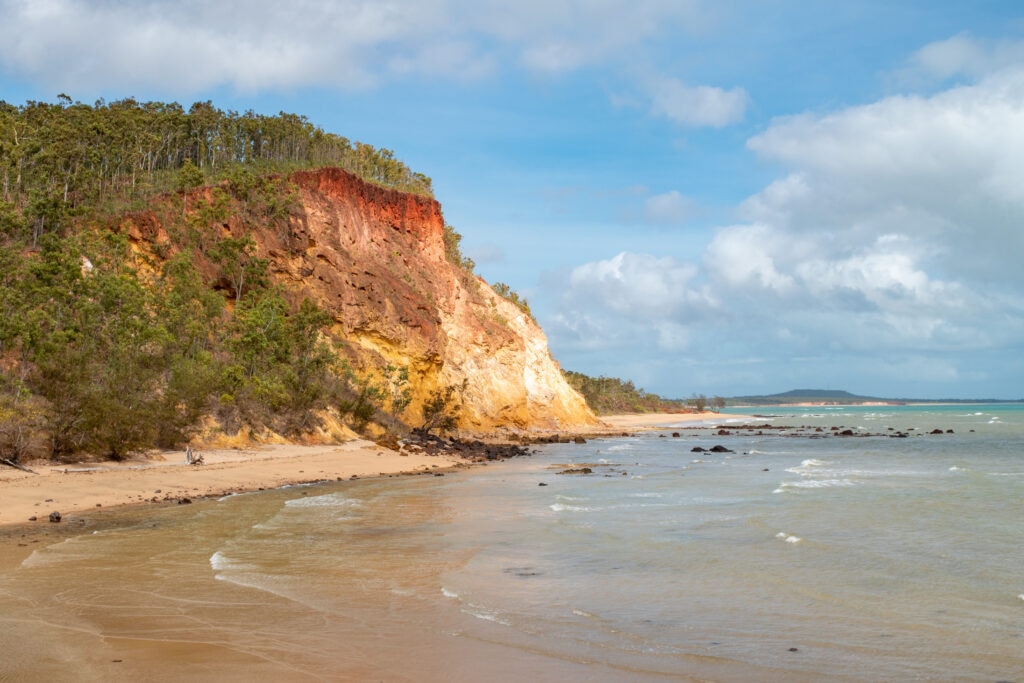 A colourful ochre cliff leads onto a white sand beach and into the ocean