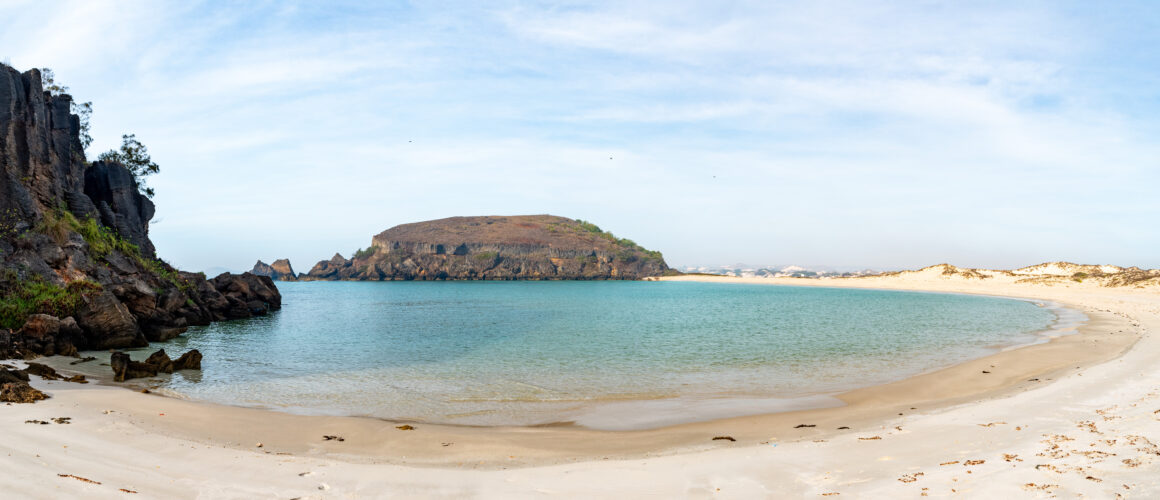 A panorama of a white sand beach looking out to the ocean and cliffs beyond