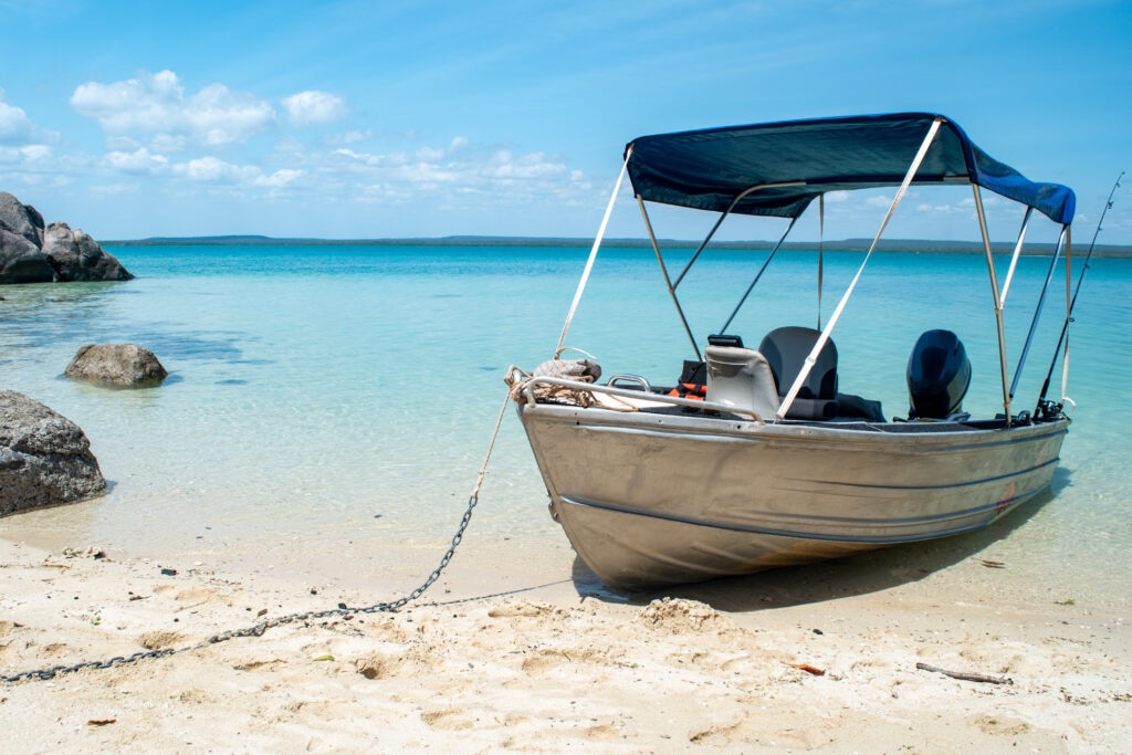 An aluminum boat sits chained on a picturesque white sand beach with granite rocks on the side