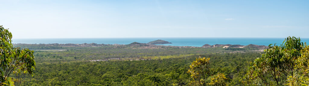 An overlook of green bushland leads to verdant dunes and blue ocean with a clear blue sky