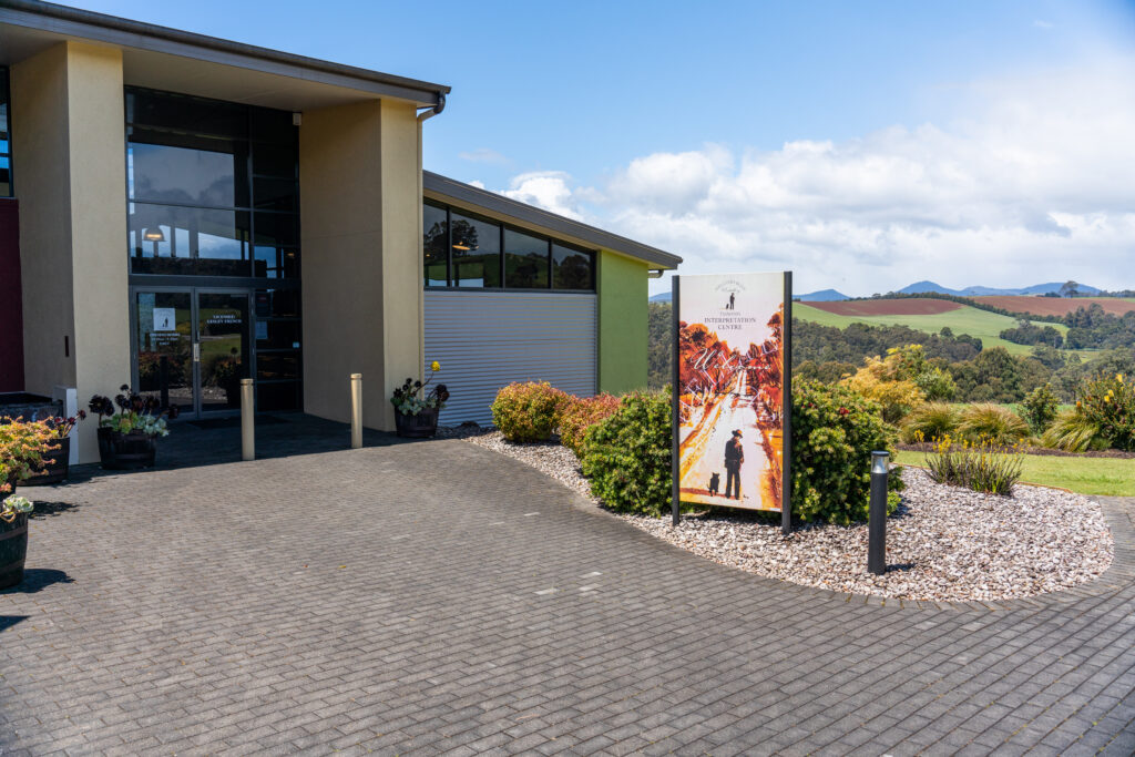 A picture of the front of Hellyers Road Whiskey Distillery with rolling farmland in the background on a mostly sunny day in Tasmania, Australia