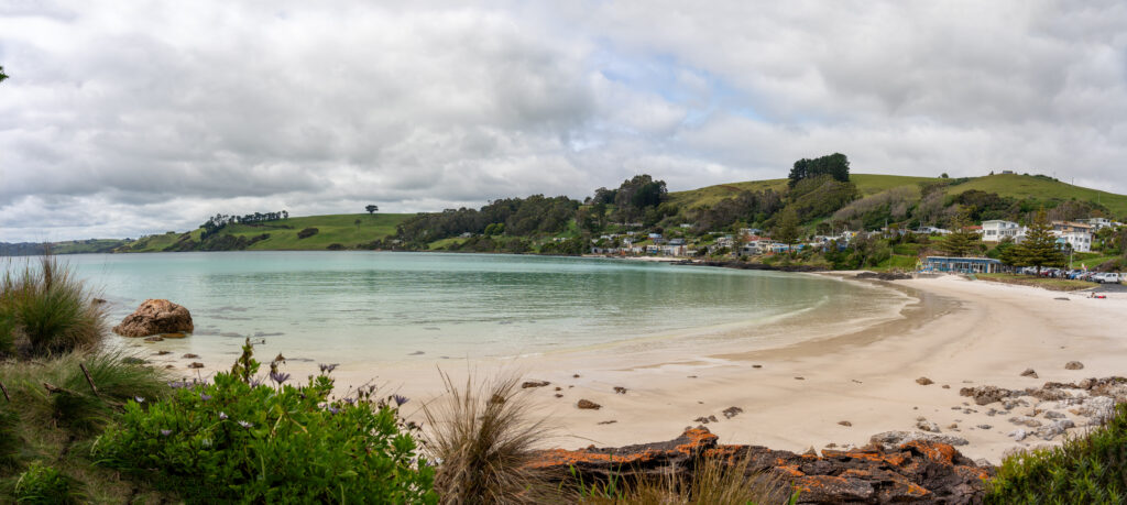 A picture of a circular oceanic bay and white sand beach known as Boat Harbour Beach, Tasmania, Australia, with hilly farmland in the background on a mostly cloudy day