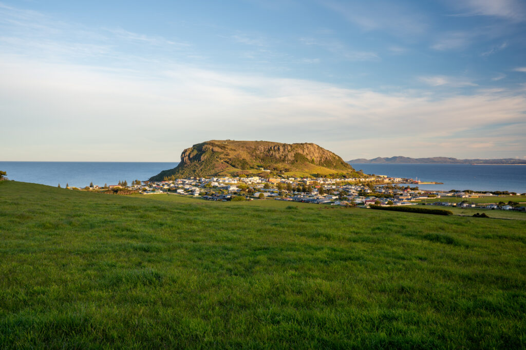 A view of the large rocky outcrop known as the Nut and township of Stanley, Tasmania, Australia from faraway with grass in the foreground at sunset