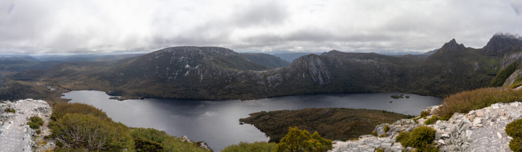 A sweeping panoramic view from high up on Marions Lookout of glacial lakes and peaks on a cloudy day in Cradle Mountain National Park, Tasmania, Australia