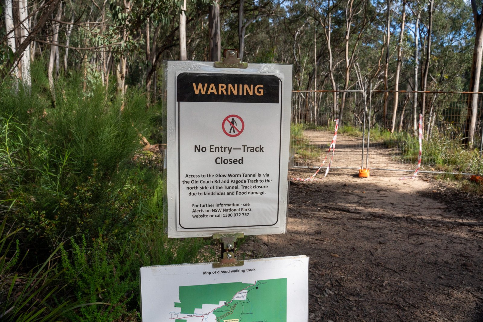 A warning sign states "no entry - track closed" and describes an alternate route to glow worm tunnel, with a fence across the track in the background