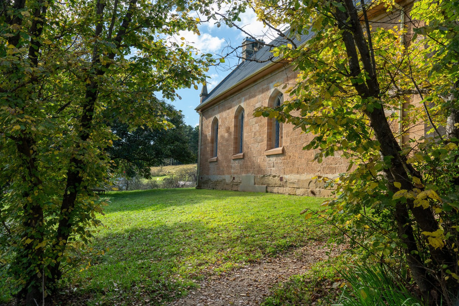 A view through the trees of a well-preserved grassy yard historic sandstone church