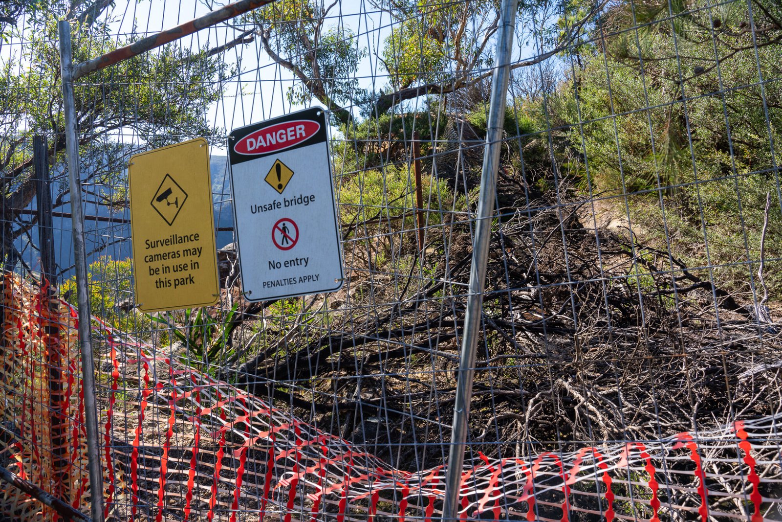 A fence with a no entry sign stands in front of a fallen tree which is blocking a dirt path