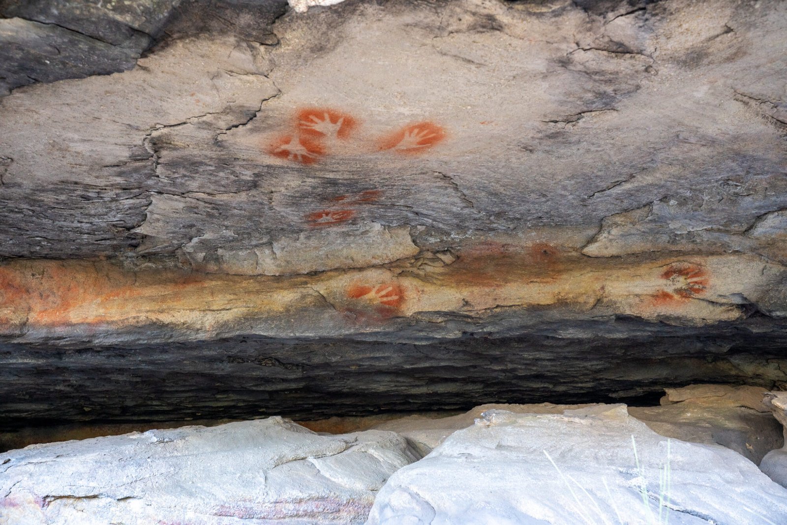 Aboriginal rock art of hand silhouettes in ochre under a rocky ledge