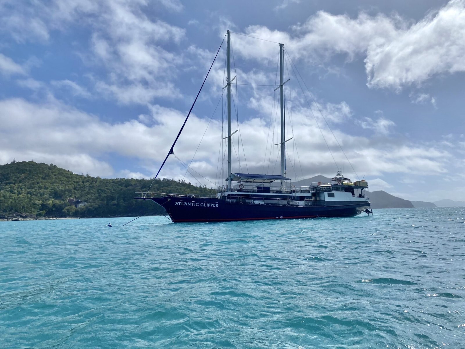 View from the water of a large sailboat with green island in the background on a partly cloudy day