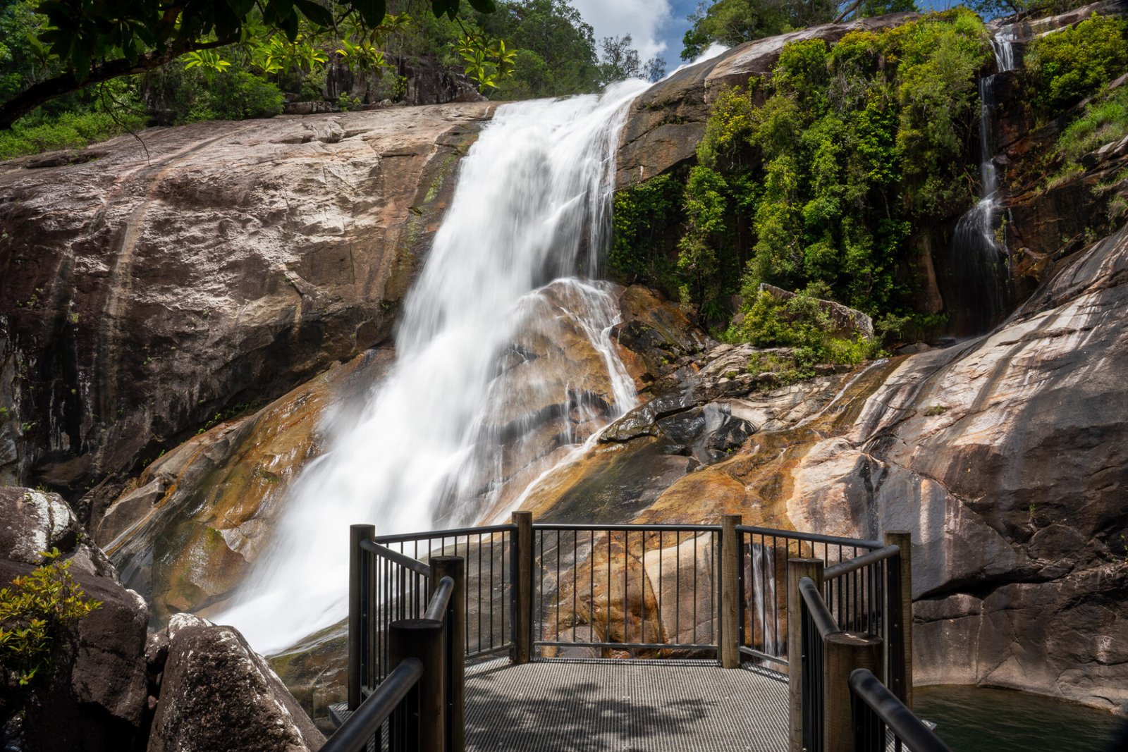 A circular viewing platform looks onto a granite rock waterfall decorated by dense green vegetation