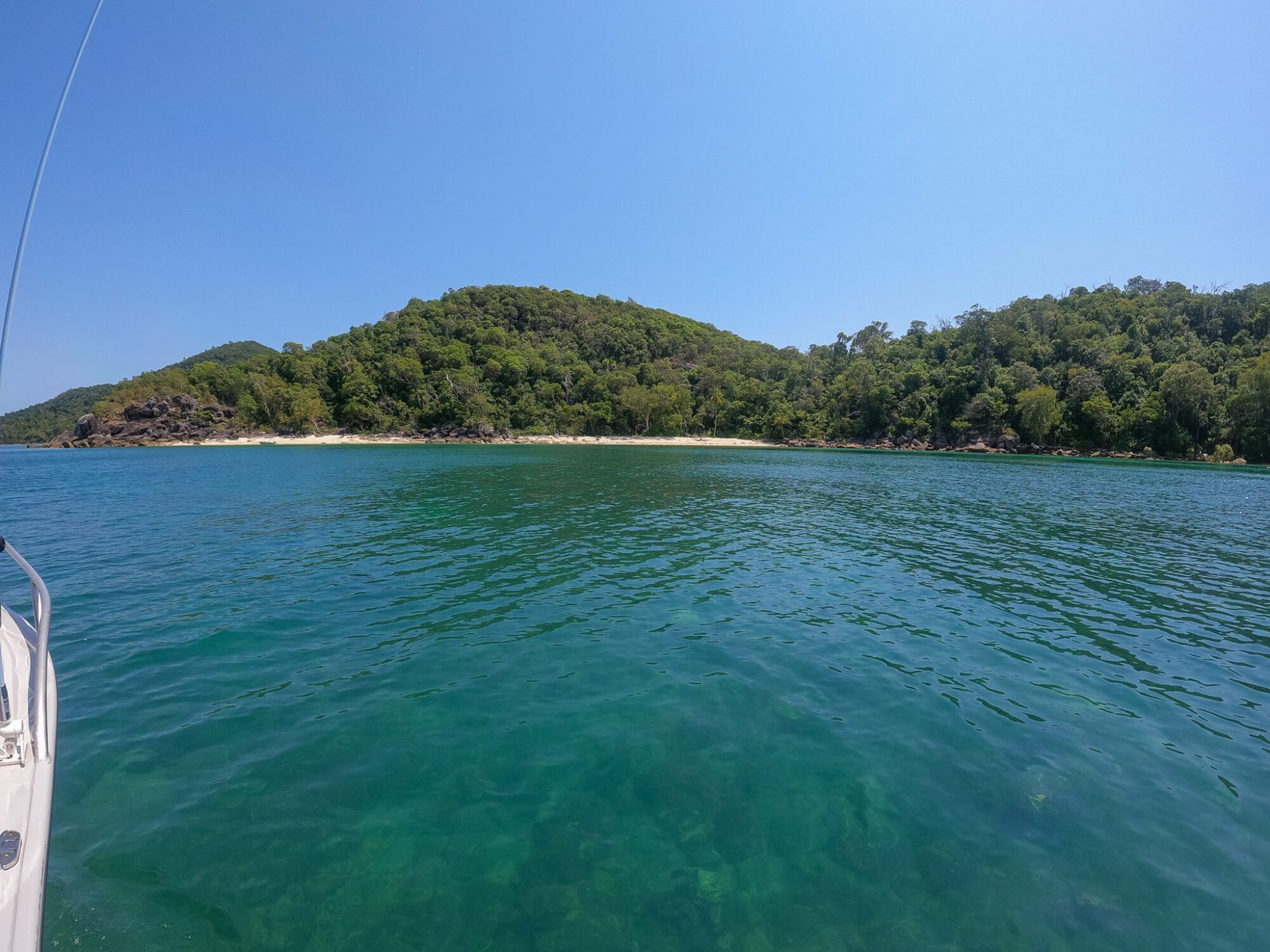 A view from a boat looking out over ocean to an island with lush green vegetation on a clear sunny day